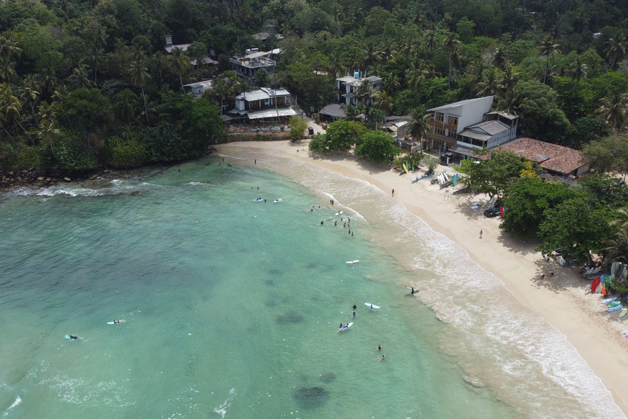 Aerial view of a turquoise bay with surfers on Sri Lanka's coast