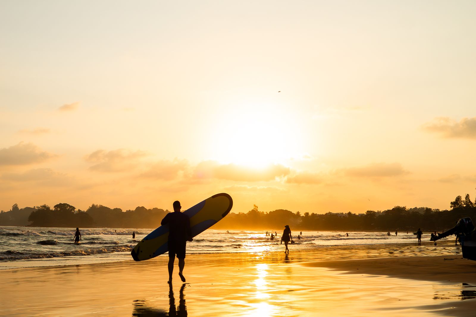 Surfer walking along Weligama beach at sunset, Sri Lanka